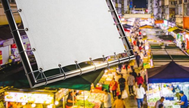 Blank white banner hanging on metal frame with grommets and cords over busy night market