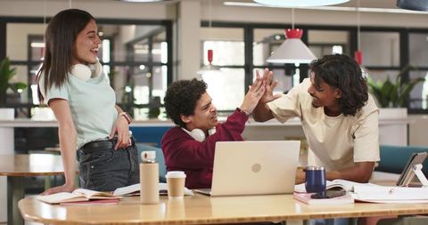 Young coworkers high-fiving after successful demo in bright open-plan coworking workspace