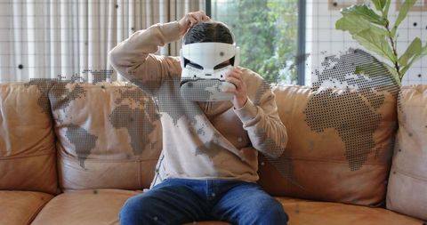 Man adjusting VR headset on leather couch with dotted world map overlay