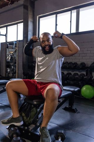 African american man flexing arms on gym bench celebrating strength training and confidence