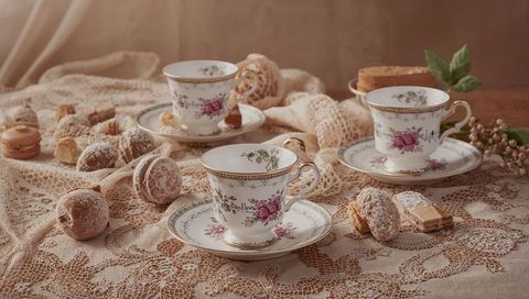 Vintage floral china teacups with gold trim on lace tablecloth with french macarons