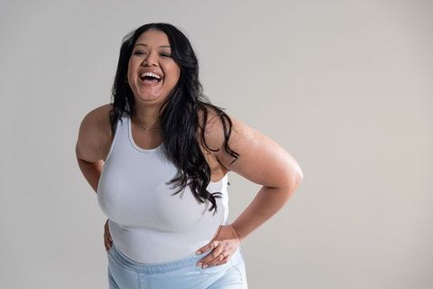 Plus-size woman laughing and leaning forward wearing white ribbed tank and light denim