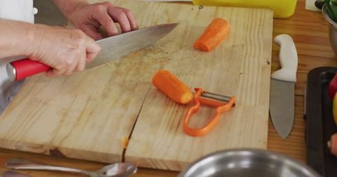 Senior Hands Slicing Carrots on Cracked Wooden Cutting Board with Chef Knife