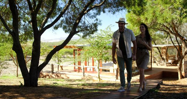A young Caucasian couple enjoys a leisurely walk along a wooden pathway surrounded by lush greenery, with copy space. Their casual attire and relaxed demeanor suggest they are on a vacation or exploring a nature reserve.