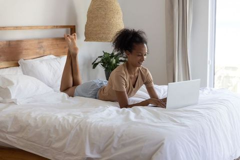 African american woman studying on laptop in bright minimalist bedroom for remote work