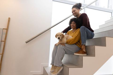 African american couple sitting on modern staircase holding golden retriever puppy