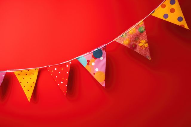 A vibrant arrangement of colorful party bunting hangs against a bright red background, perfect for adding a festive touch to any party or celebration event. Ideal for use in promotional materials for events, birthday parties, or festive seasons, this image exudes joy and excitement, enhancing invitation cards, party flyers, and celebratory web content.
