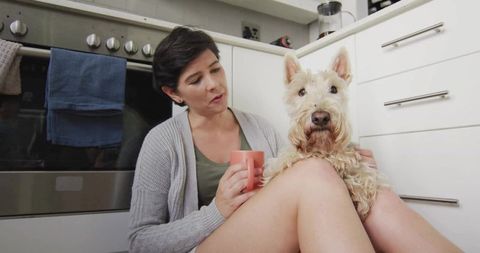 Woman relaxing in minimalist kitchen with terrier on lap