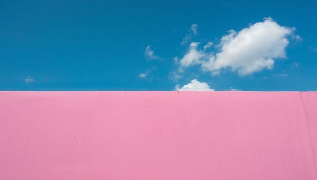 Pastel pink facade against cyan sky with cumulus clouds - minimalist colorblock architecture