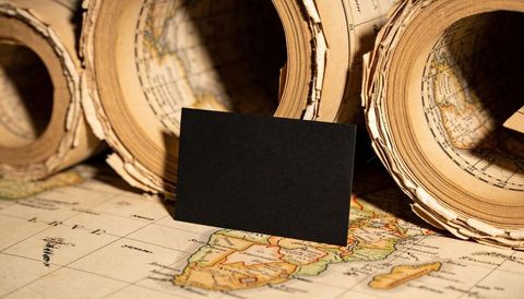 Blank black card standing on aged southern africa map, rolled atlases glowing under warm lamp