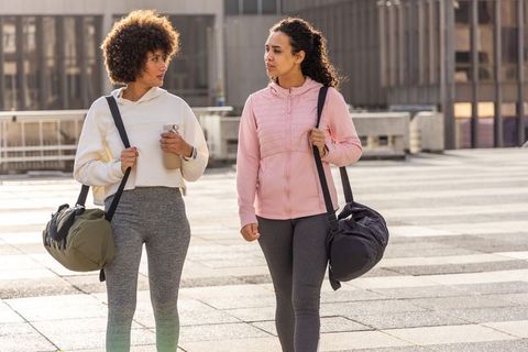 Multicultural women walking and talking post-workout carrying duffel bags and water bottle