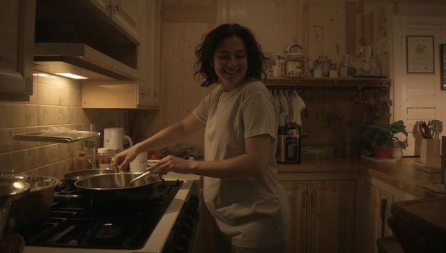 Smiling woman stirring skillet on gas stove in cozy rustic wooden kitchen evening