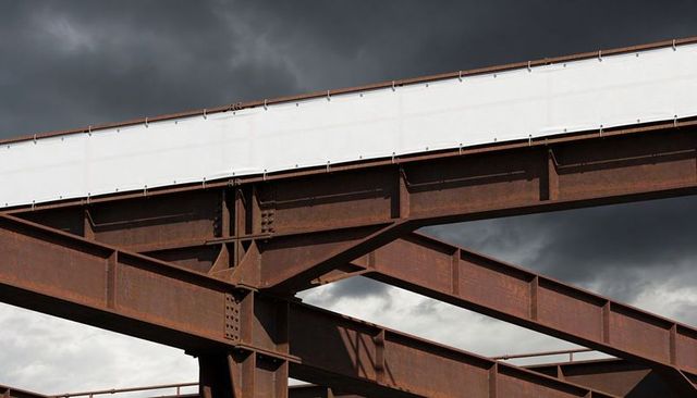Rusted industrial girders forming dramatic geometric lines beneath stormy sky