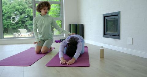 African american yoga instructor guiding student into childs pose in sunlit home studio