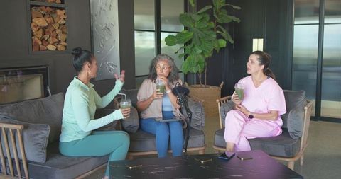 Three women chatting over green smoothies with podcast microphone in cozy lounge