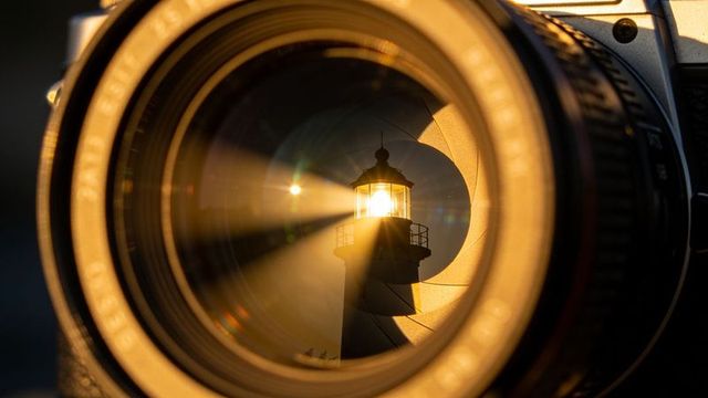 Golden lighthouse beam framing through camera lens aperture iris with flare