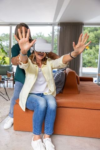 Senior Woman Experiencing Virtual Reality Guided by Daughter in Modern Living Room