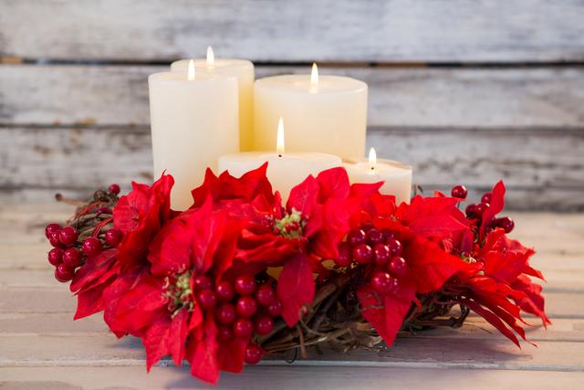 Christmas candles surrounded by red poinsettia flowers and berries on a wooden plank. Ideal for holiday greeting cards, festive home decor inspiration, seasonal blog posts, and Christmas-themed advertisements.