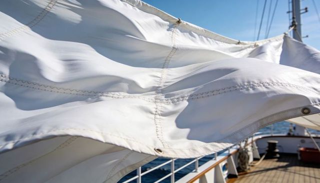 Billowing white mainsail catching wind with stitched seams and grommets on yacht deck