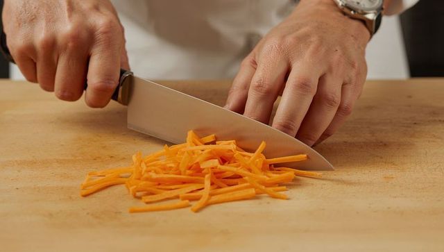 Male hands cutting carrots into julienne strips with chef knife on wooden cutting board