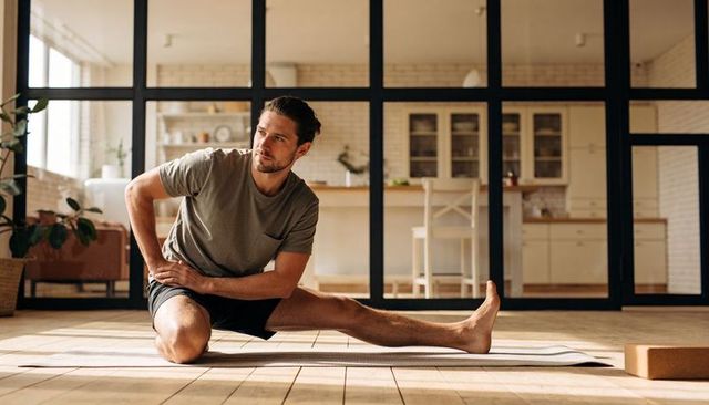 Man stretching on yoga mat in sunlit modern apartment, home wellness routine