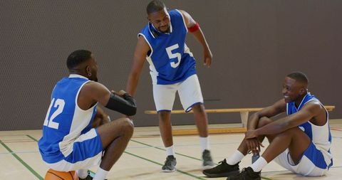 Basketball teammates sharing handshake and smiling on indoor gym court, team camaraderie