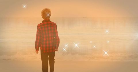 Back view child standing on sunset beach wearing red plaid flannel watching calm sea sparkle