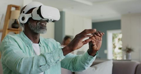 Senior African American Man Exploring Virtual Reality at Home Wearing VR Headset Gesturing