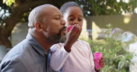 Father and daughter blowing bubbles outdoors in summer garden