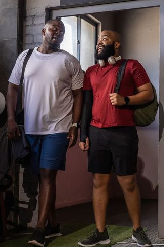 Two friends chatting while leaving gym carrying duffel and backpack, wearing headphones
