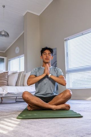 Asian man meditating at home on green yoga mat practicing mindfulness and inner calm