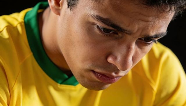 Focused young athlete looking down wearing yellow and green jersey, dramatic moody closeup portrait