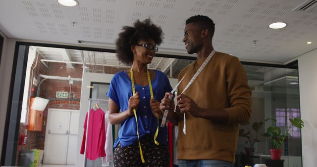 African ameriacan man and woman having fun measuring fabrics in fashion workshop environment. Perfect for articles on sewing, teamwork in fashion industry, or promo material for clothing retail businesses. Emphasizes collaboration, happiness, and creativity in professional setting.
