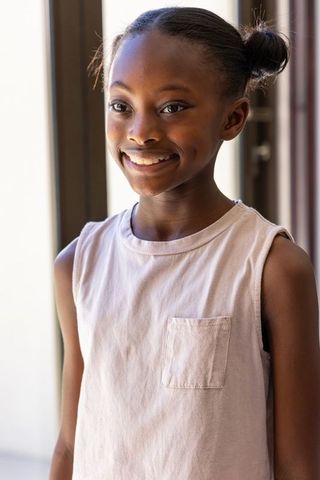 African girl smiling by window showing dimples wearing casual tank top in soft natural light