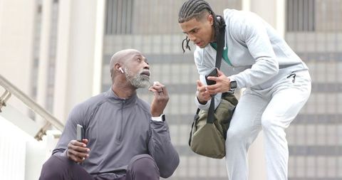 Young trainer advising older athlete on urban steps, discussing workout plan