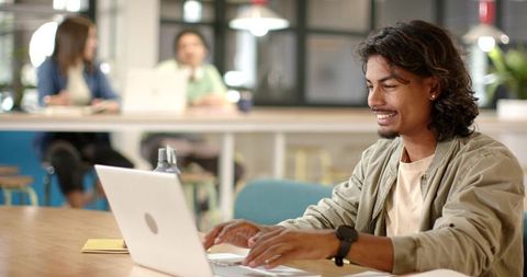 Young African American man working on laptop in contemporary coworking lounge, smiling