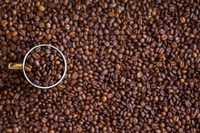 Cup filled with coffee beans surrounded by a pile of roasted coffee beans. Useful for coffee shop promotions, beverage advertisements, or websites focused on coffee culture. Highlighting rich and aromatic aspect of freshly roasted coffee beans, suitable for posters or backgrounds.