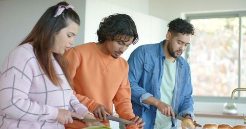 Friends chopping vegetables and assembling sandwiches at bright modern kitchen counter