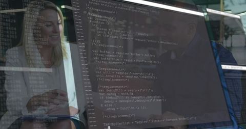 Colleagues reviewing code on monitor while holding notepad, collaborating in modern office