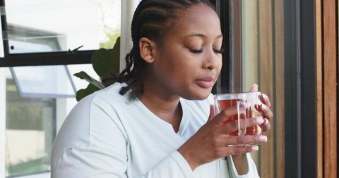 African american woman enjoying warm tea by sunny window in minimalist home