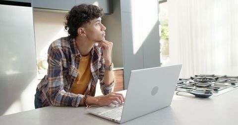 Young man working on laptop in modern kitchen setting