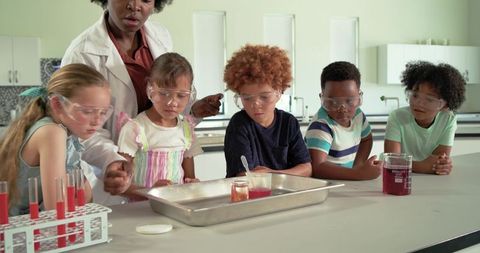Teacher guiding diverse children conducting hands-on chemistry experiment in school lab