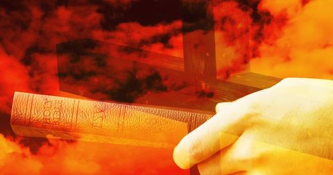 Silhouette of Cross with Hand Holding Bible Against Fiery Sky