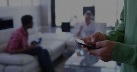 Person Using Smartphone with Friends Socializing in Living Room Setting