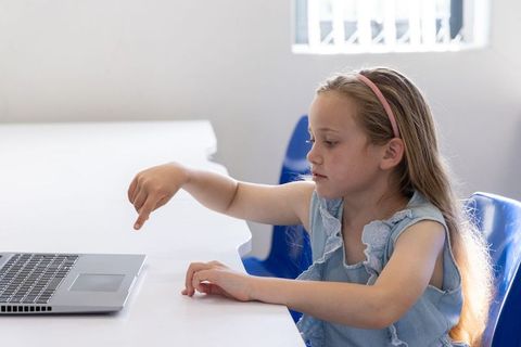 Schoolgirl pointing at laptop during classroom computer activity with focused expression