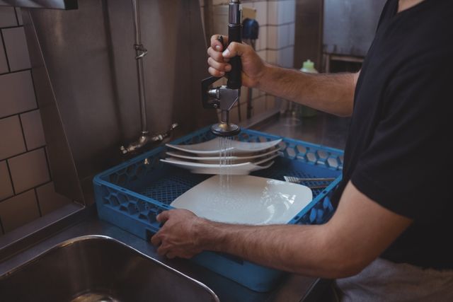 Mid section of washing plates at sink in commercial kitchen
