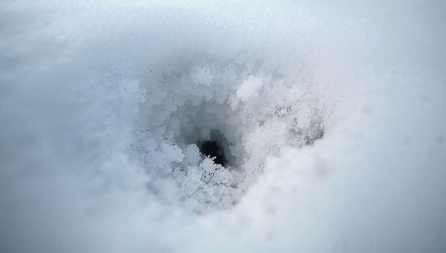 Macro frost cavity in snow revealing ice crystal rim and dark void, blue winter texture