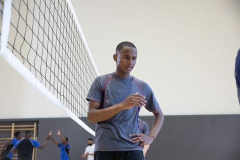 African american male adjusting shirt standing at net during indoor volleyball practice