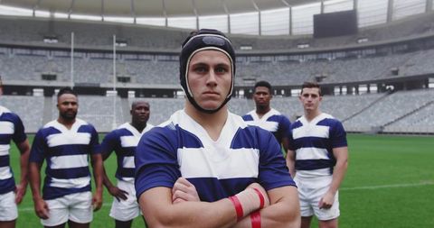 Rugby captain standing arms crossed leading team stadium turf wearing blue white stripes