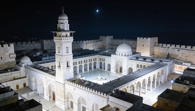 Moonlit historic mosque courtyard with minaret and arched colonnades at night